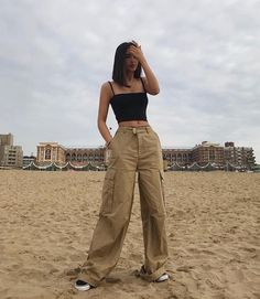 a woman standing on top of a sandy beach next to a tall building and holding her head