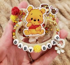 a hand holding a baby bear brooch with flowers and beads on it's side