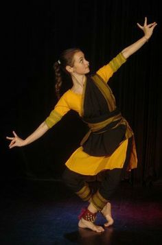 a woman in a yellow and black dress is doing a dance move with her arms outstretched