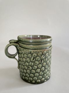 a green ceramic cup sitting on top of a white table