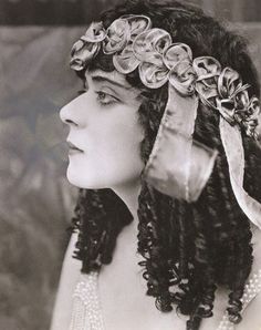 an old fashion photo of a woman with curly hair wearing pearls and ribbon around her head