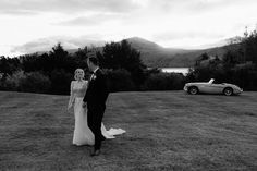 a bride and groom standing in front of a sports car on the grass at their wedding