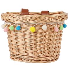 a wicker basket with pom - poms hanging from the handle and leather straps