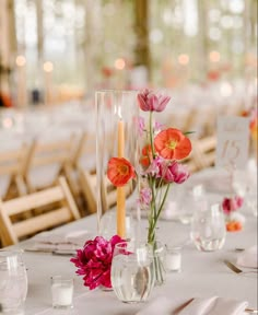 flowers in vases and candles are on the table at a wedding reception with white clothed tables