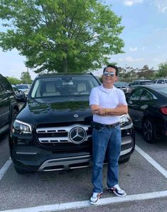 a man standing in the parking lot next to a black mercedes benz suv with his arms crossed