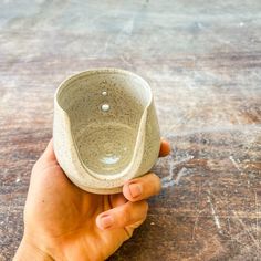 a hand holding a small cup on top of a wooden table