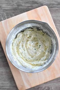 a metal bowl filled with white sauce on top of a wooden cutting board