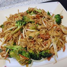 a white plate topped with noodles and broccoli on top of a countertop