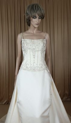 a mannequin wearing a white wedding dress in front of a brown curtained background