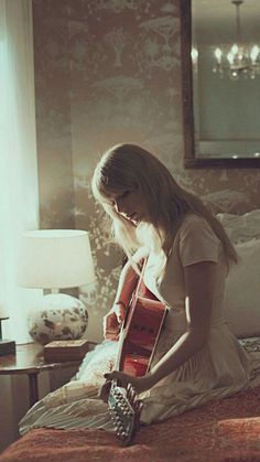 a woman sitting on top of a bed with a book in her hand and a lamp next to her