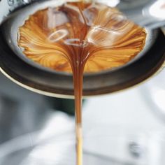 caramel colored liquid being poured into a coffee cup with spoons in the foreground