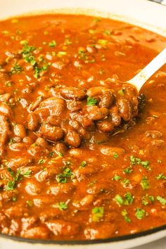 a spoon full of beans and parsley on top of a pot filled with sauce