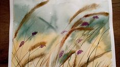 a watercolor painting of grass and flowers on a piece of paper that is sitting on a table