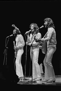 the bee gees performing on stage with microphones in front of their heads and hands