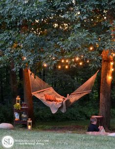 a hammock hanging in the middle of a forest with lights strung over it