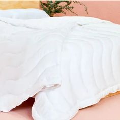 an unmade bed with white sheets and pillows on top of it, next to a potted plant