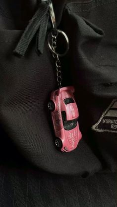 a pink toy car keychain hanging from a black jacket with a tag on it