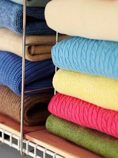 several folded towels are stacked up in a rack on top of other folded towels and blankets