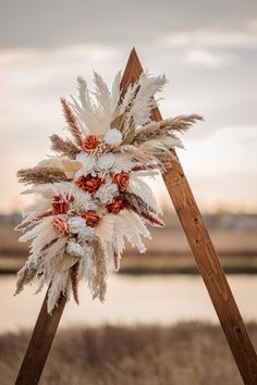 an arrangement of flowers and feathers is placed on top of a easel in front of a body of water