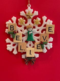 a christmas ornament hanging on a red wall with words believe and an angel