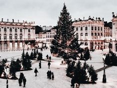 a large christmas tree is in the middle of a courtyard with people walking around it