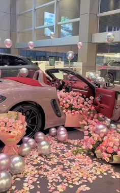 a pink sports car parked in front of a bunch of balloons and flowers on the ground