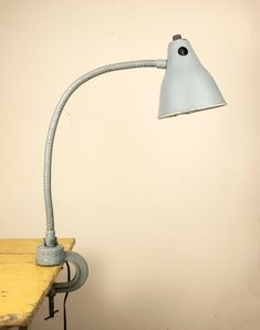 a desk lamp sitting on top of a wooden table next to a white wall with a light blue shade