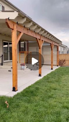 an outdoor covered patio area with grass and wooden posts on the side of the building