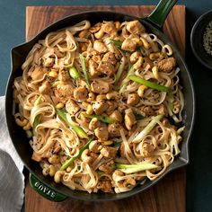 a skillet filled with noodles and meat on top of a wooden cutting board next to a bowl of seasoning