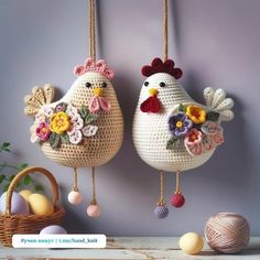 two crocheted chickens hanging from hooks next to an egg basket with eggs in it