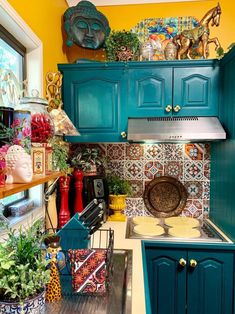 a kitchen with blue cabinets and colorful tile backsplash, potted plants on the counter