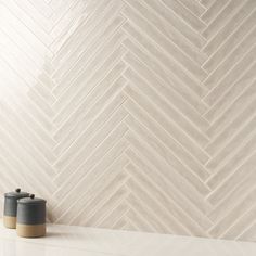 two coffee cups sitting on top of a counter next to a white wall with herringbone pattern