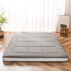 a mattress on the floor in front of a window with curtains and potted plants