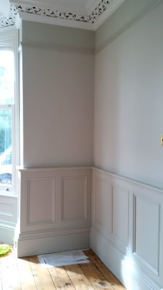 an empty room with white walls and wood flooring in the corner, along with a window