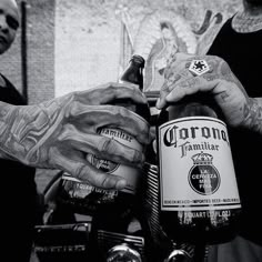 two men with tattooed arms holding beer bottles in front of each other and one has his arm wrapped around another man's hand