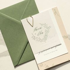 an open green envelope with a white wedding card and a gold heart brooch on it