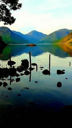 a lake with mountains in the background and rocks on the water's edge at sunset