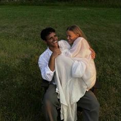 a man holding a woman in his arms while sitting on a bench outside at sunset