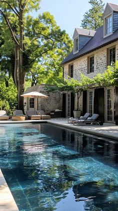 an outdoor swimming pool with lounge chairs and umbrellas next to the house in the background