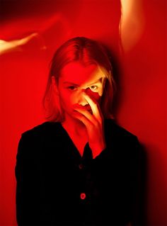 a woman is holding her hand to her face and looking at the camera with red light behind her