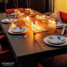 a long table with plates and candles on it in front of a fire place setting