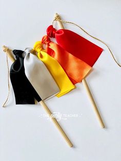 three small flags are tied to wooden sticks on a white surface, one with a red bow and the other with a yellow ribbon