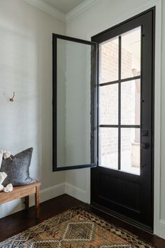 a room with a rug, mirror and bench in front of the door that is open