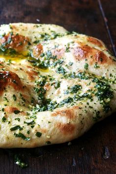 a close up of a pizza on a wooden table with cheese and herbs sprinkled on it