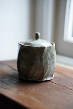 a ceramic container sitting on top of a wooden table next to a window sill