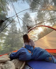 a woman sitting in a sleeping bag on top of a blue tarp with trees in the background