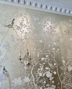 the wall paper has birds and flowers on it, while two candelabras stand in front of them