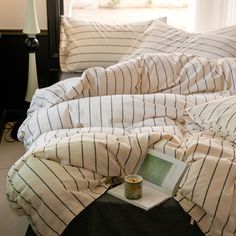 an unmade bed with white and black striped comforter, pillows and a book on it