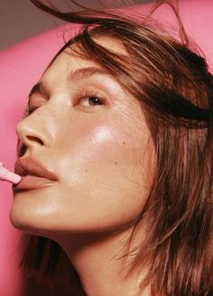 a woman is brushing her teeth with a pink toothbrush in front of her face