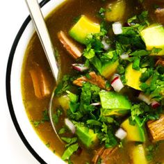 a bowl of soup with meat, vegetables and other things in it on a white surface